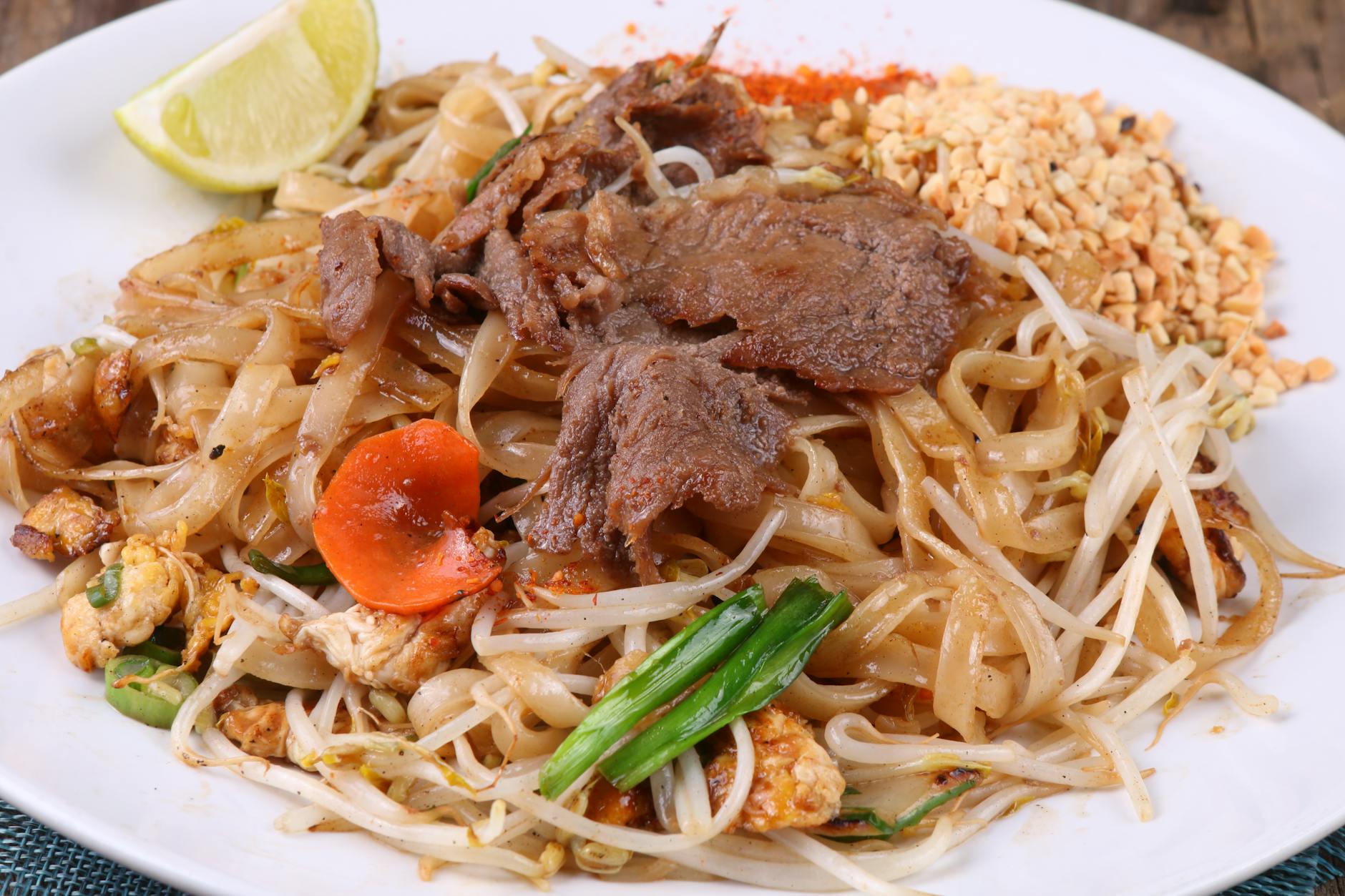 Pad Thai z wołowiną, warzywami, orzeszkami i limonką na białym talerzu