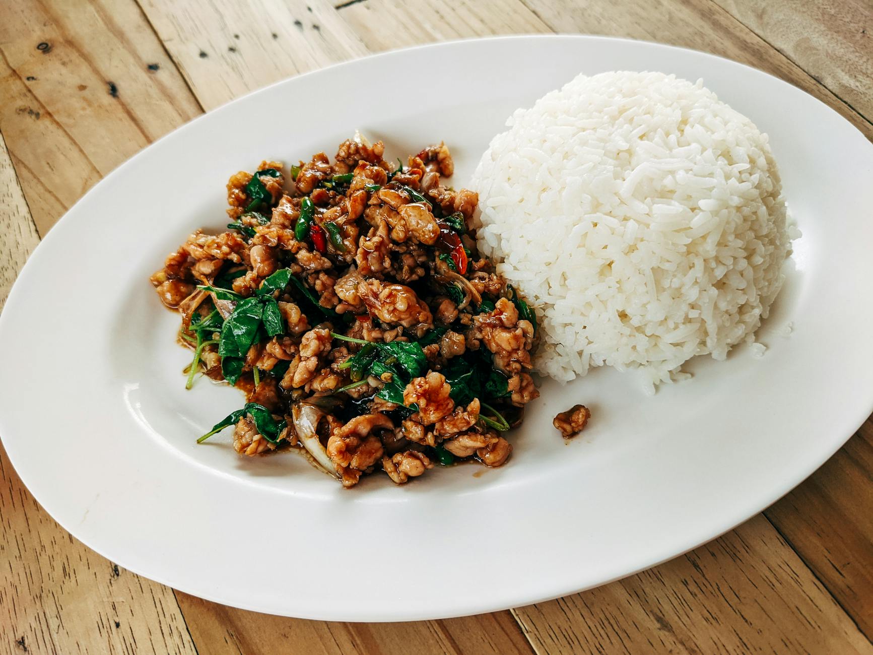 Tajskie stir fry z wieprzowiną, bazylią i ryżem na drewnianym stole Tajskie stir fry z wieprzowiną, bazylią i ryżem na drewnianym stole