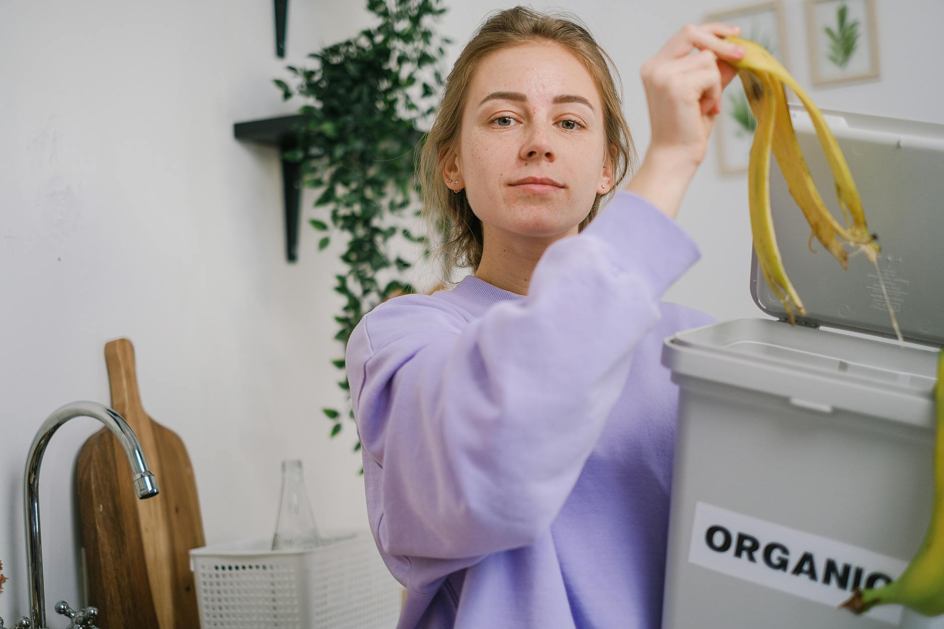Kobieta wrzuca skórkę banana do pojemnika na bioodpady w kuchni