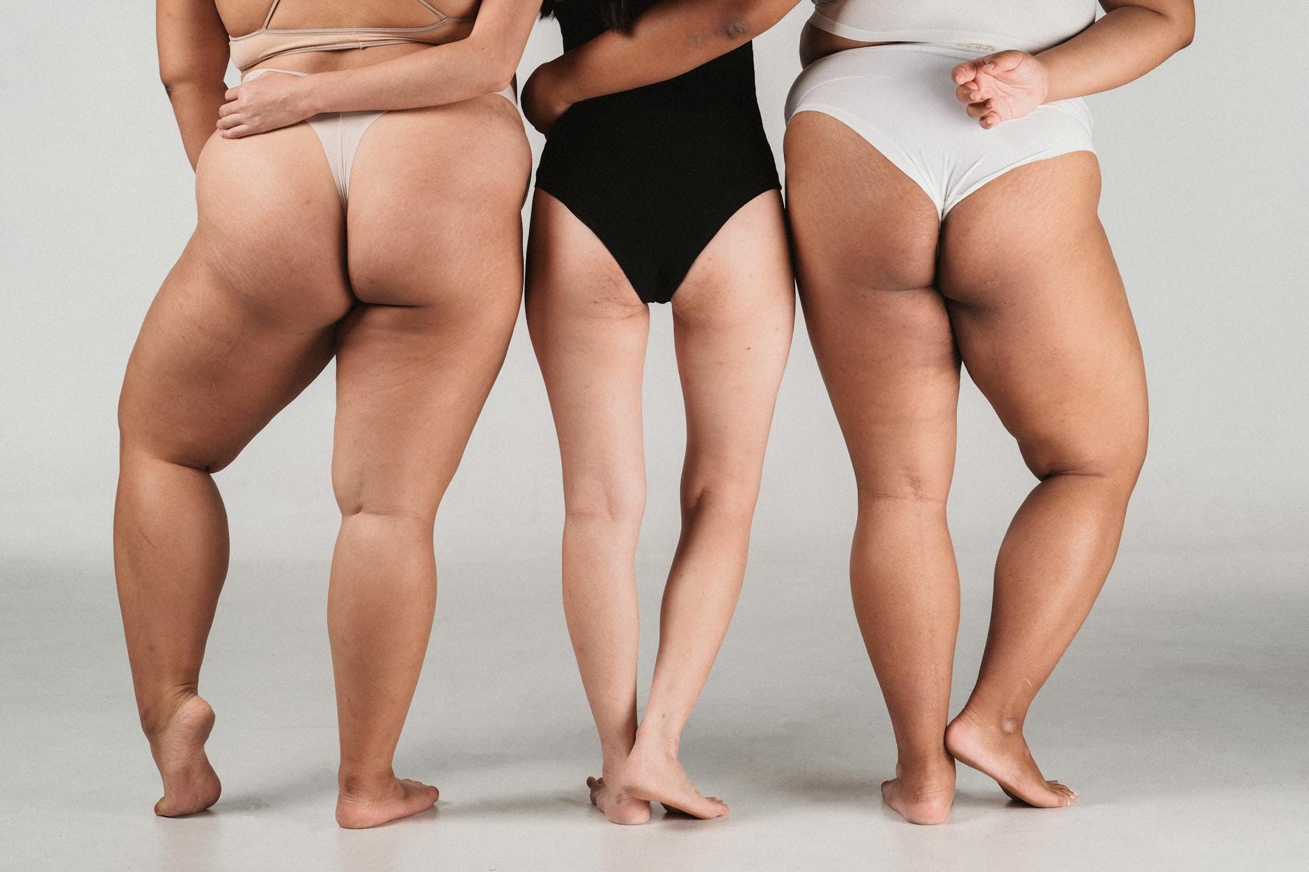 Modelki o szczupłej i puszystej sylwetce obejmujące się tyłem w studio