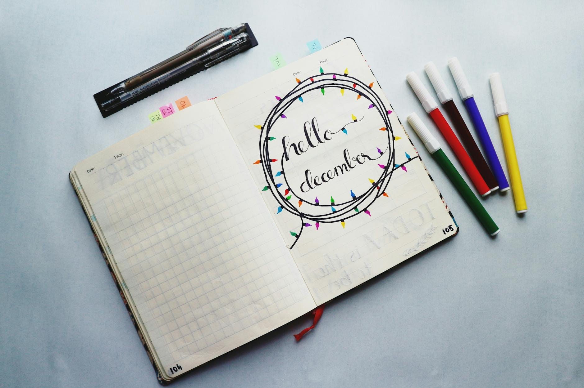 Otwarty planner z napisem Hello December i kolorowymi markerami dookoła
