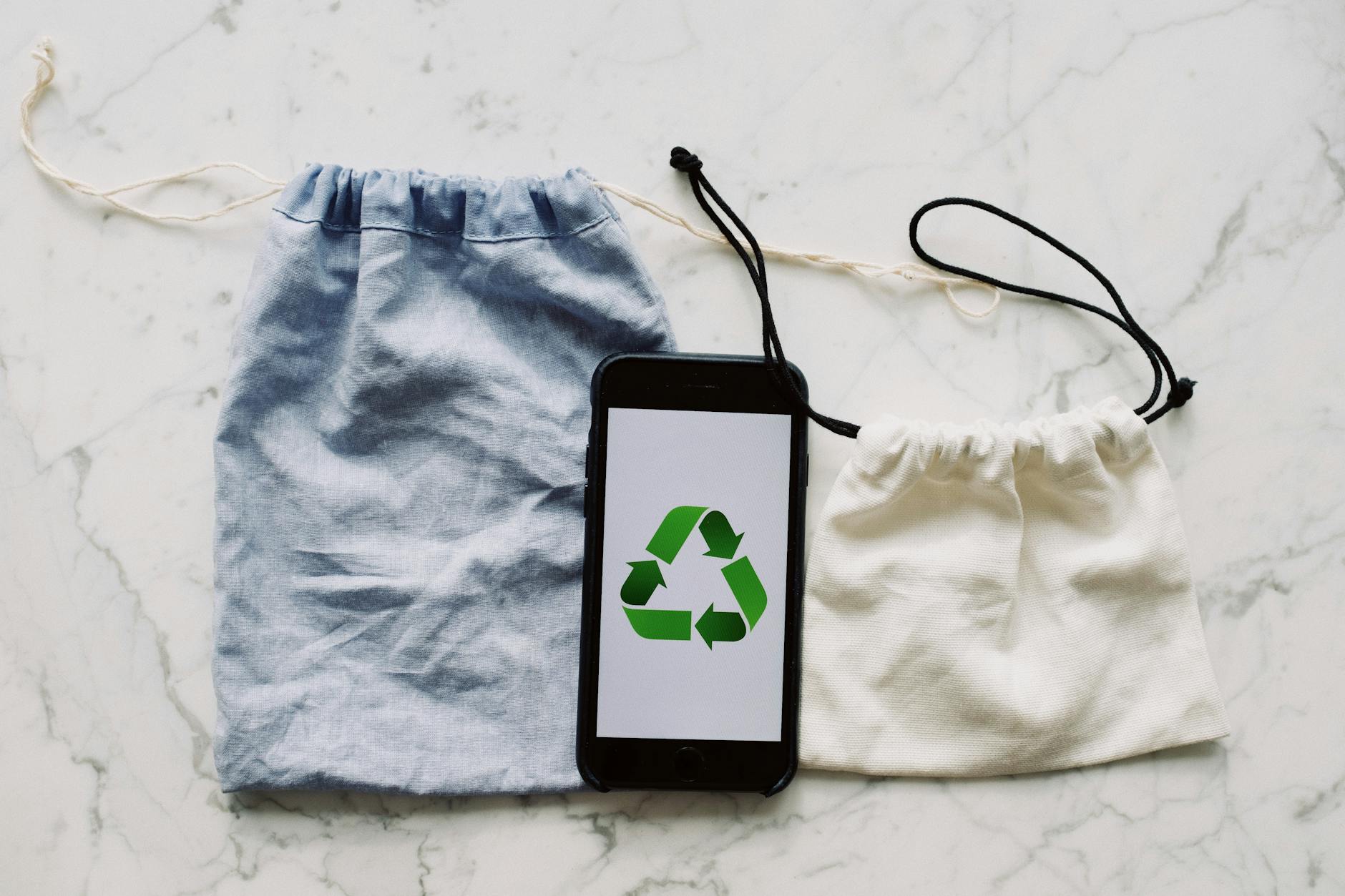 Smartfon z symbolem recyklingu między płóciennymi torbami na stole