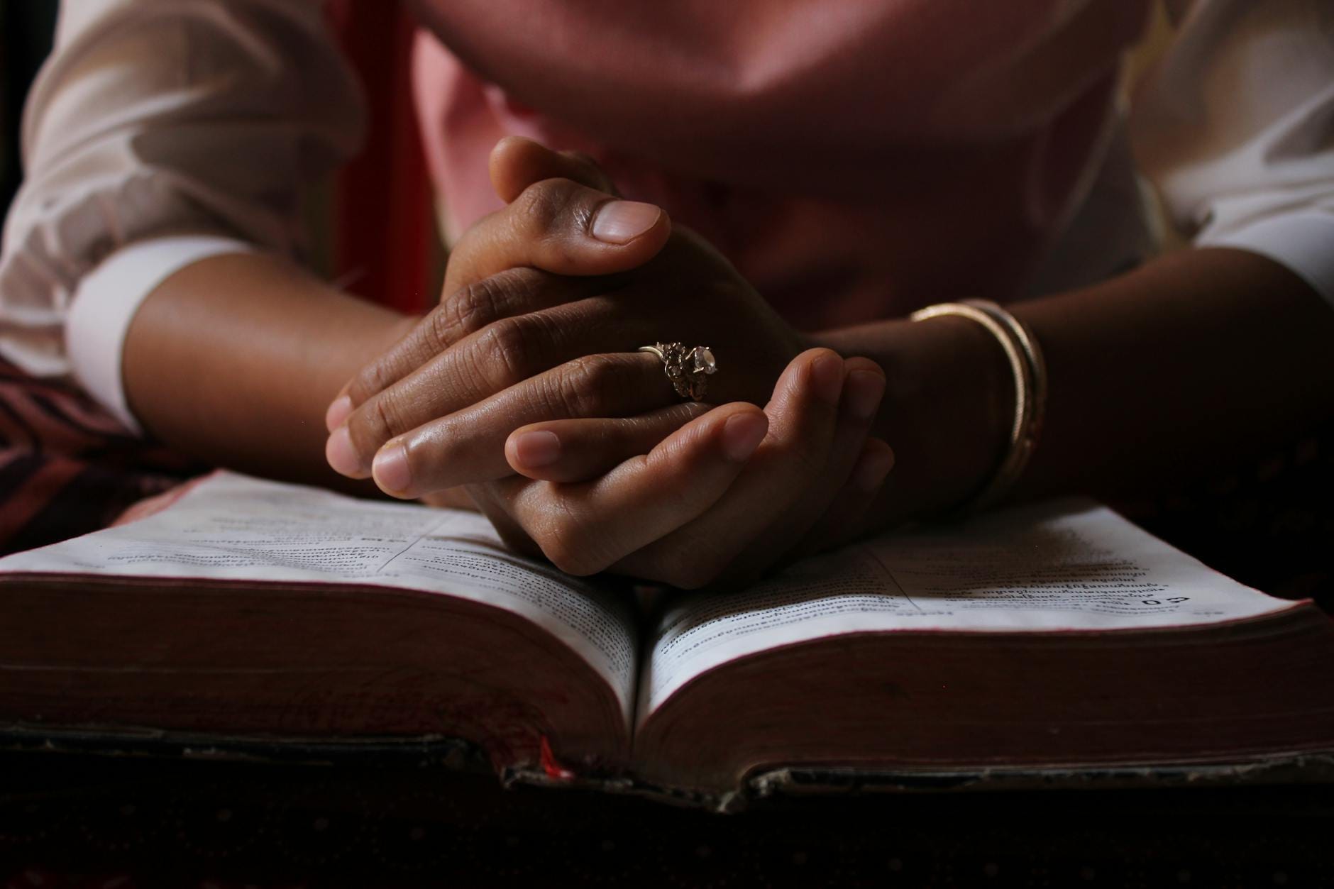 Złożone dłonie w modlitwie nad otwartą Biblią podczas osobistej lektury